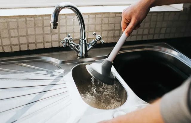 A person is using a plunger to clean a kitchen sink.