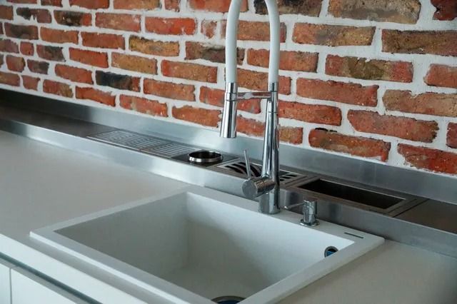 A kitchen sink with a brick wall behind it