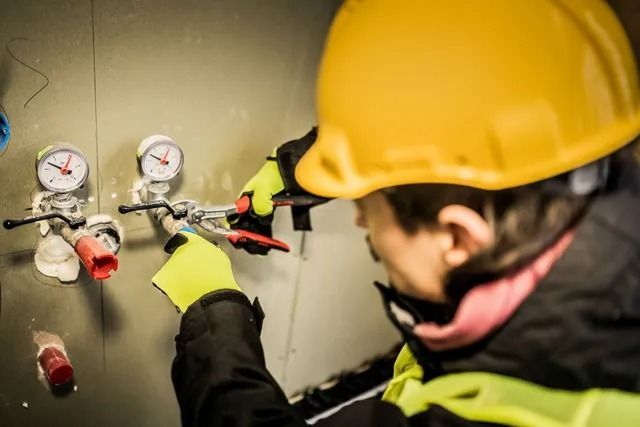 A man wearing a yellow hard hat is working on a pipe.