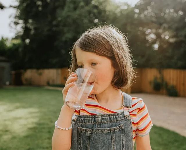 A little girl is drinking a glass of water outside.