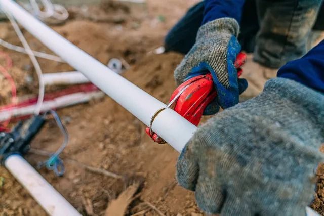 A person is cutting a plastic pipe with a pipe cutter.