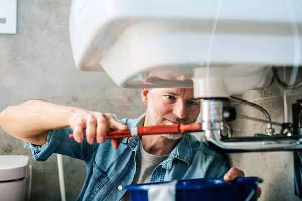 A man is fixing a sink with a wrench in a bathroom