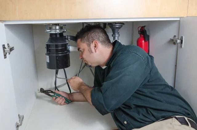 A man is fixing a garbage disposal under a sink.