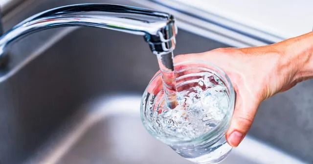 A person is pouring water into a glass from a faucet.