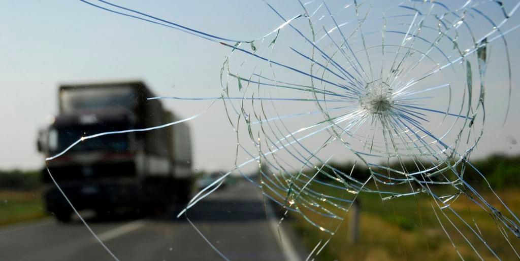 A truck is driving down a highway with a broken windshield.