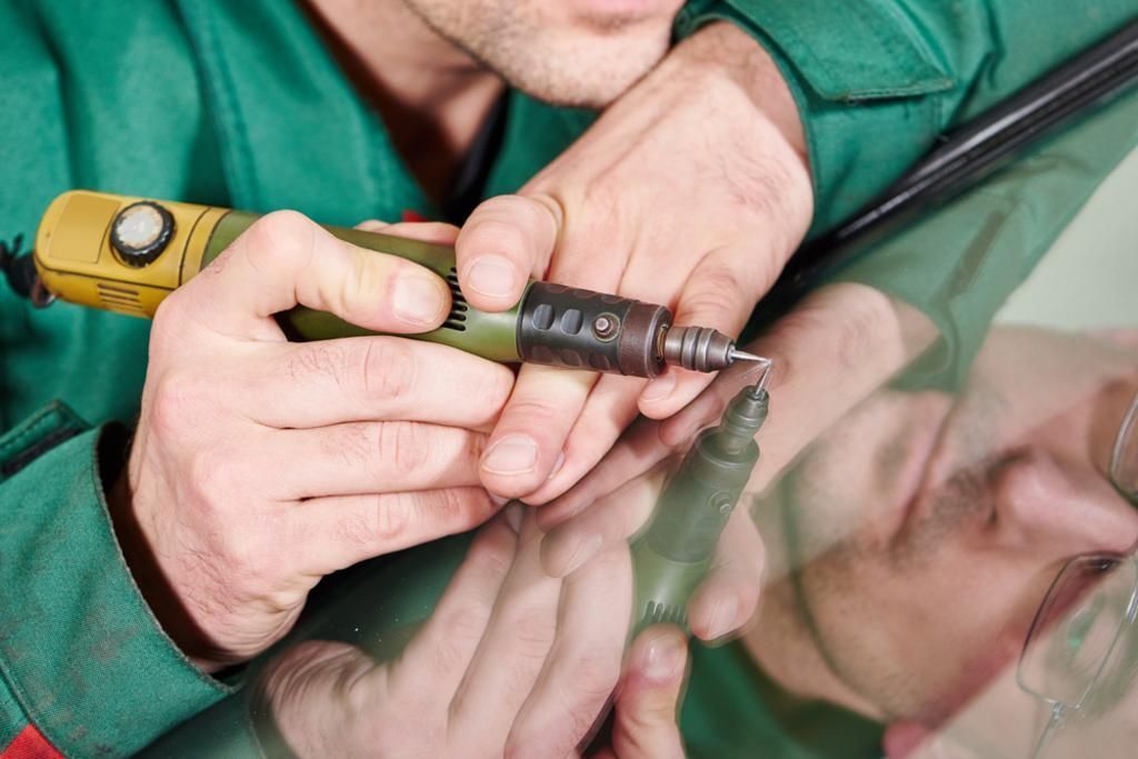 A man is working on a car windshield with a grinder.