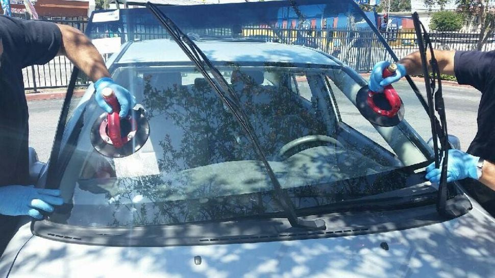 Two men are installing a windshield on a car.