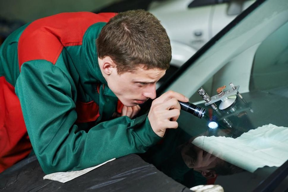 A man is looking at a car windshield.