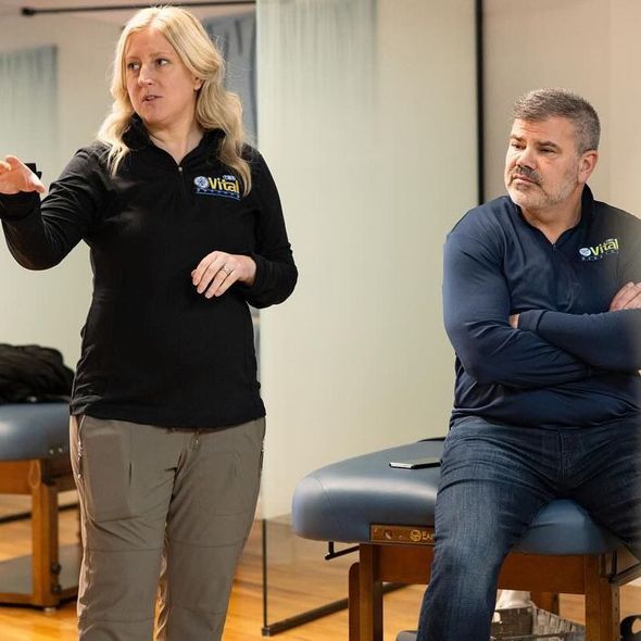 A woman is standing next to a man who is sitting on a stool.