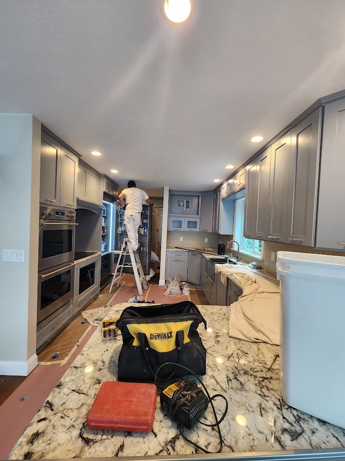 Kitchen renovation in progress with workers on ladders, tools, and cabinets along a narrow galley kitchen.