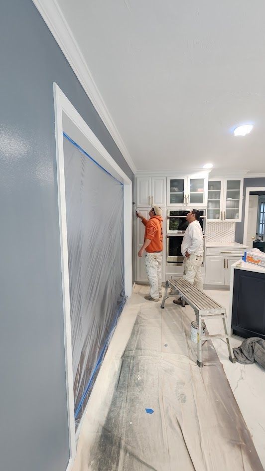 Workers painting a hallway, with blue wall trim and masking tape along the floor and walls