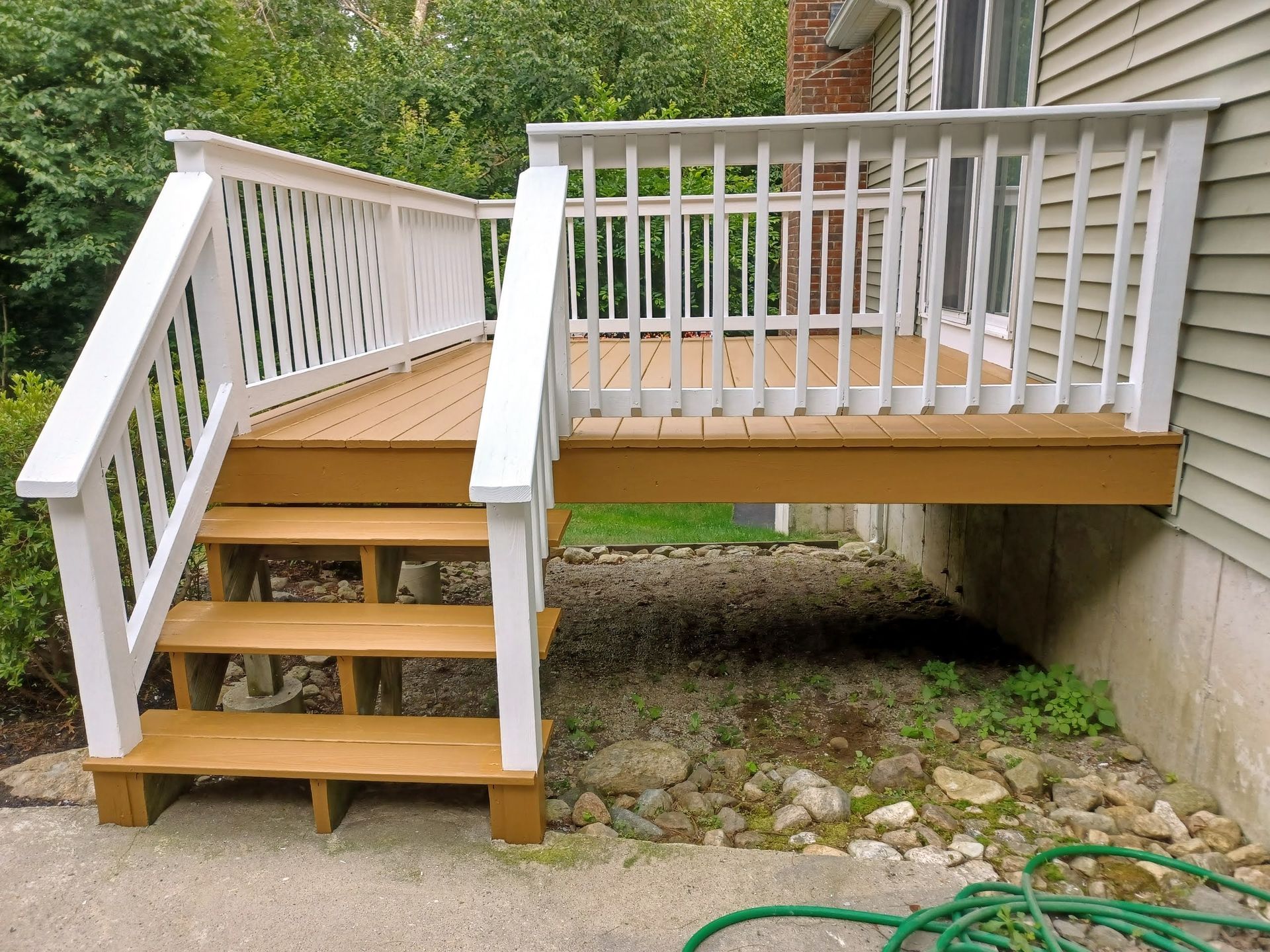 Empty tan deck with white railings and stairs leading up to a porch