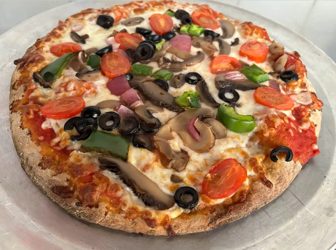 A pizza with tomatoes , mushrooms , peppers , olives and cheese on a plate.