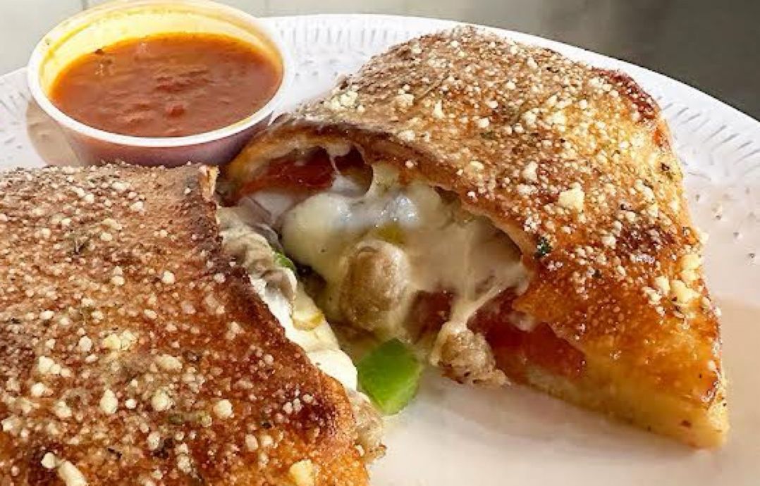 A close up of a pizza sandwich on a paper plate with a dipping sauce.