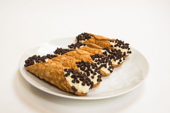 Three cannoli with chocolate chips on a white plate.