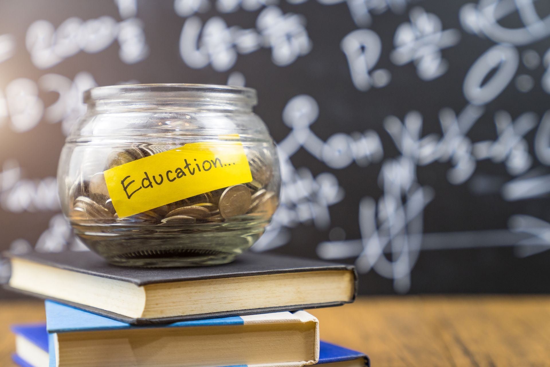 A jar filled with coins is sitting on top of a stack of books.