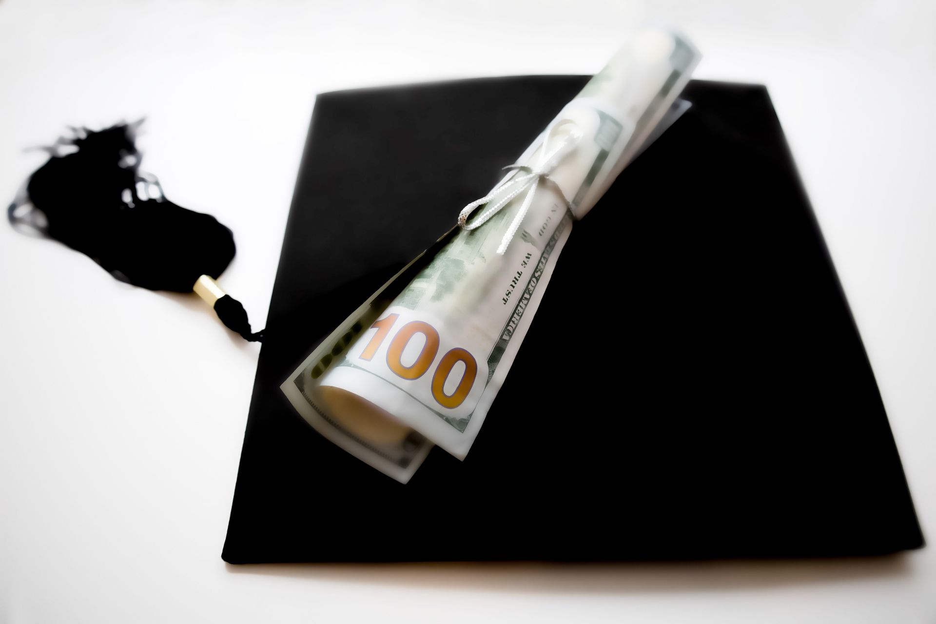 A roll of 100 dollar bills on top of a graduation cap