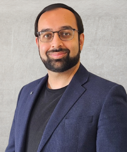 A man with a beard wearing glasses and a blue jacket