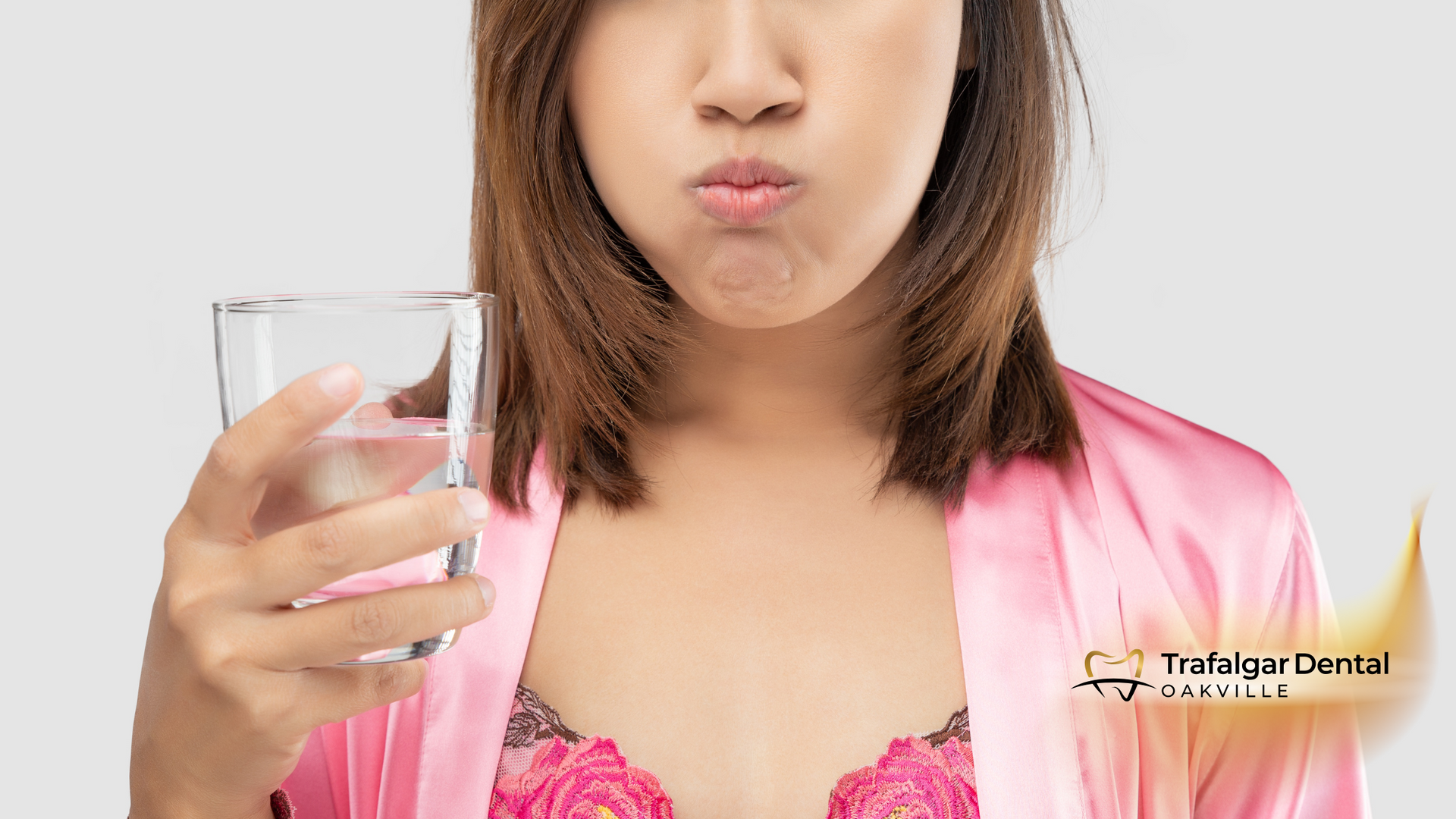 A woman in a pink robe is holding a glass of water in her mouth.