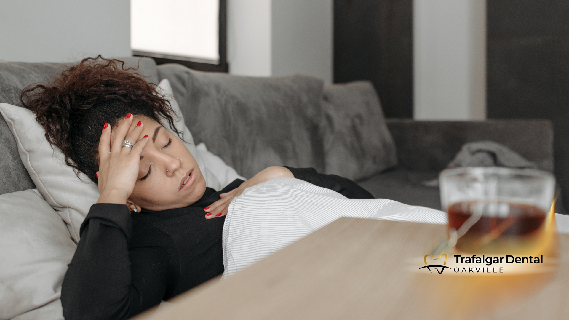 A woman is laying on a couch with her hand on her forehead.
