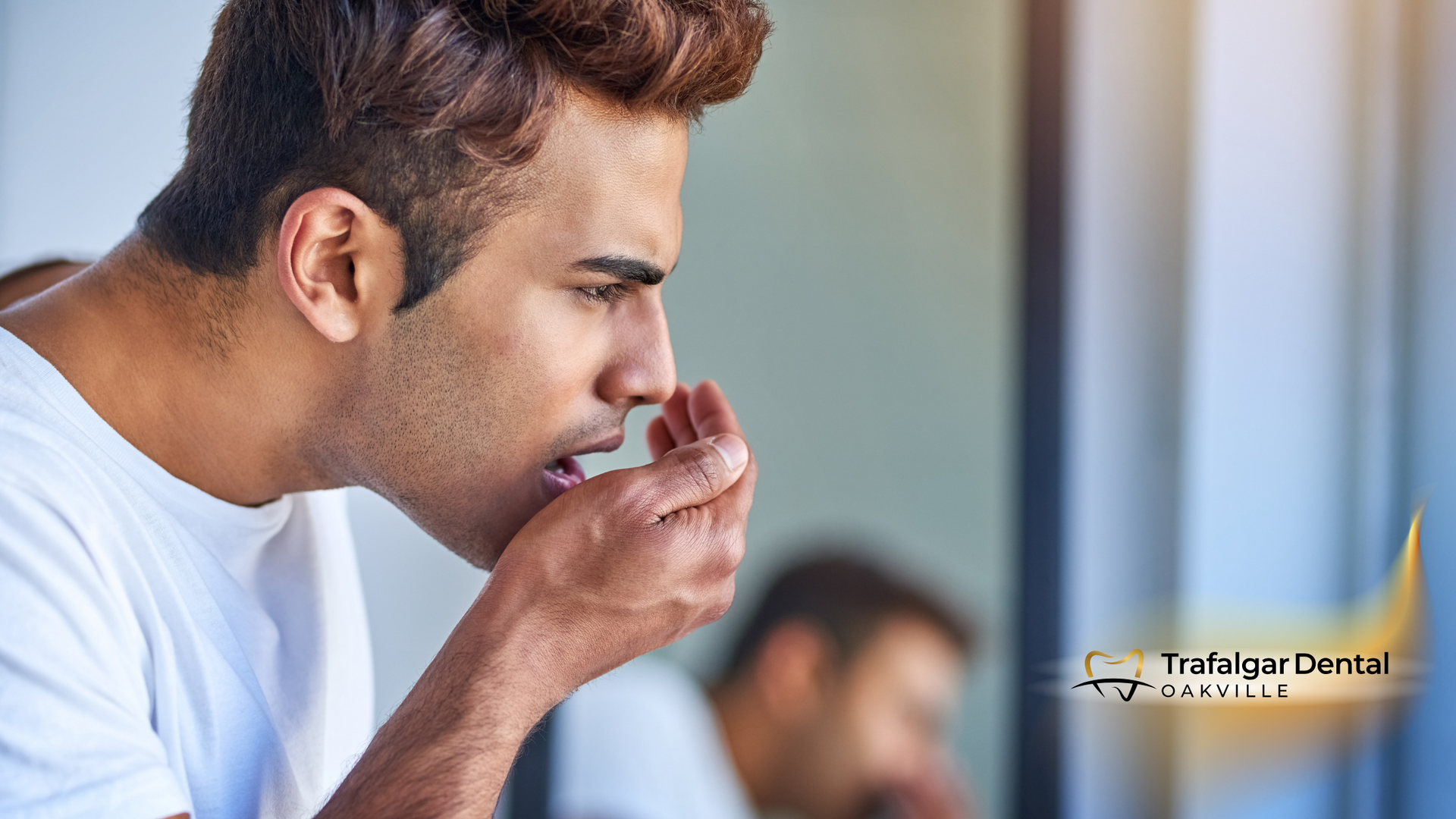 A man is covering his mouth with his hand while looking in the mirror.