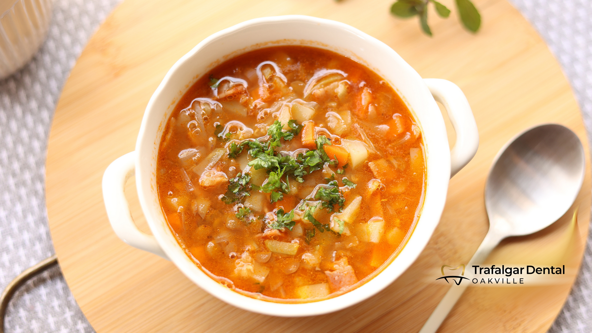 Soup in a white bowl on a wooden board, with a spoon to the side.