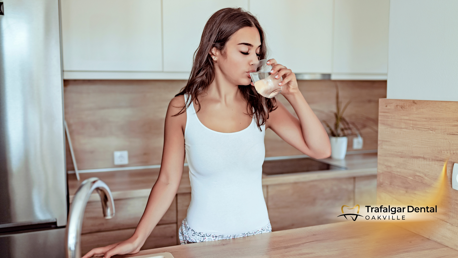 Woman in a kitchen drinking from a glass, standing near a sink.