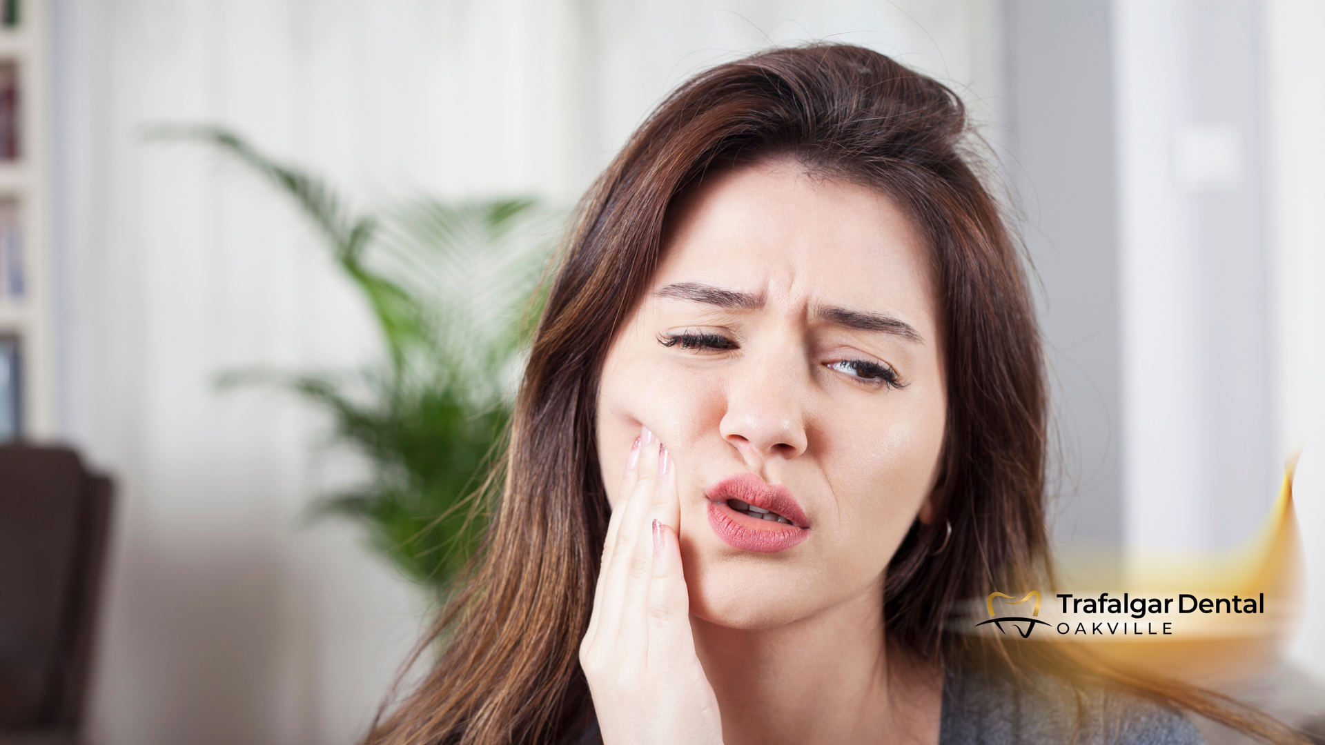 Woman with a pained expression, hand on cheek, likely experiencing tooth pain.