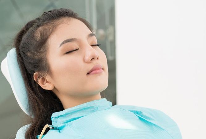 A woman is laying in a dental chair with her eyes closed.