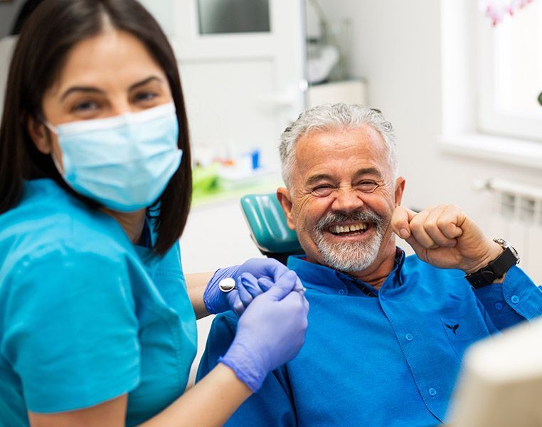 A man is sitting in a dental chair while a female dentist examines his teeth.