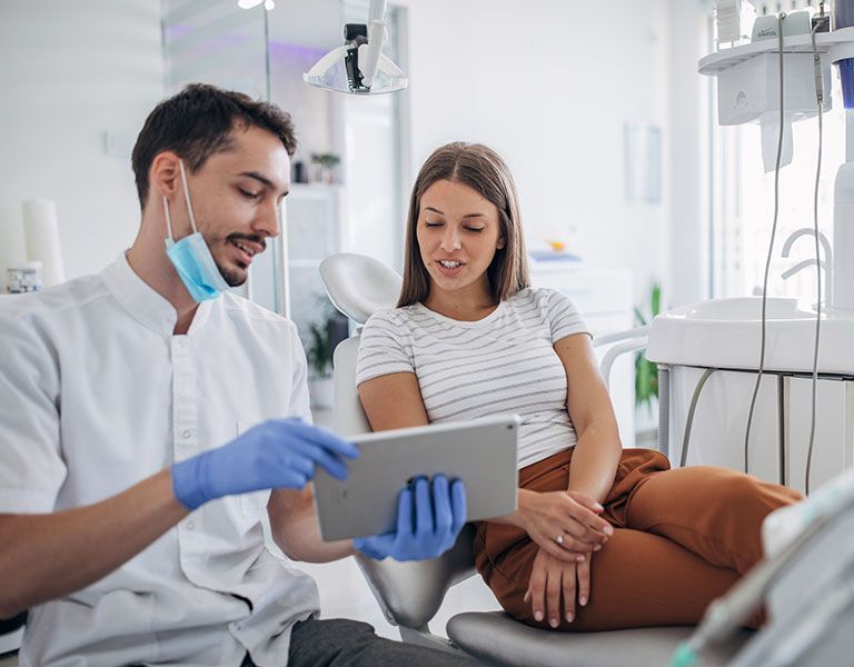 A dentist is showing a tablet to a patient in a dental chair.