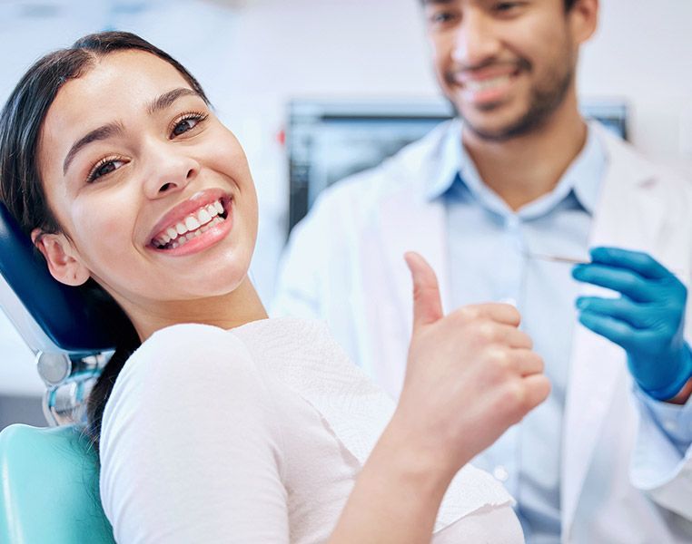 A woman is giving a thumbs up while sitting in a dental chair.