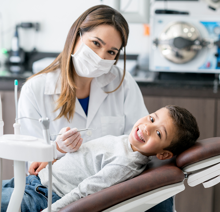 A little boy is laying in a dental chair with a dentist wearing a mask.