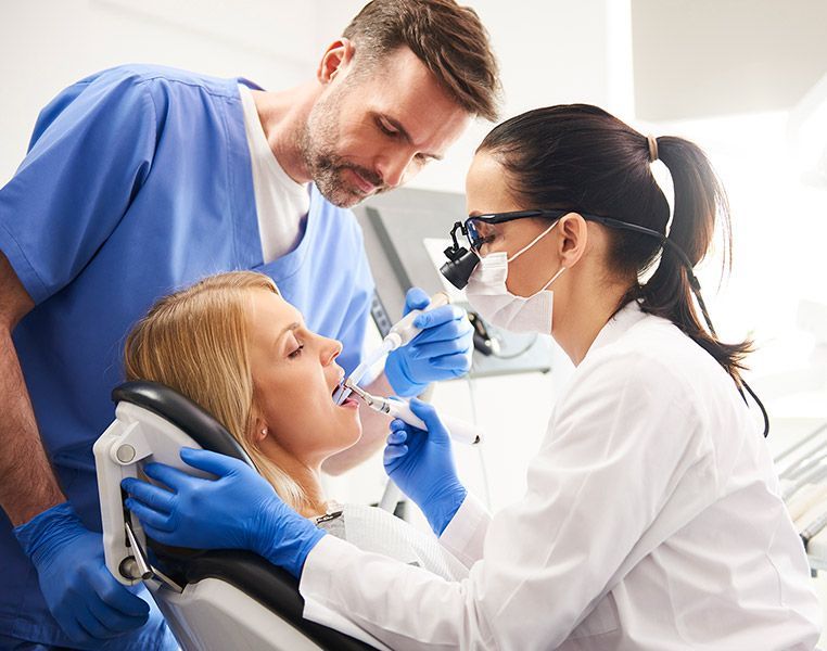 A woman is sitting in a dental chair getting her teeth examined by two dentists.