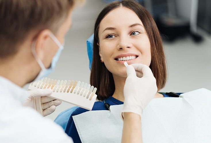 A woman is sitting in a dental chair while a dentist examines her teeth.