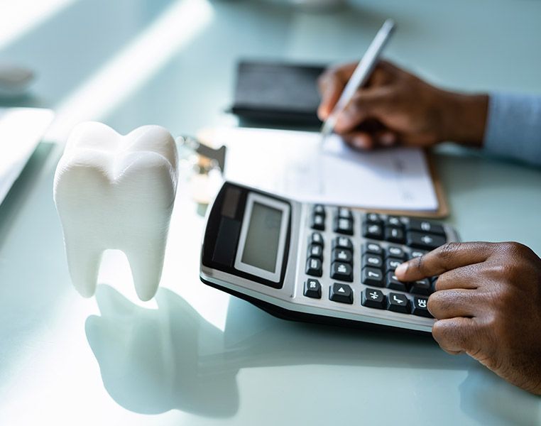 A person is using a calculator next to a tooth model.