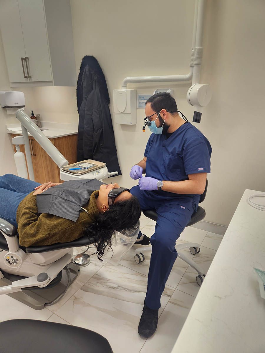 A woman is laying in a dental chair while a dentist examines her teeth.