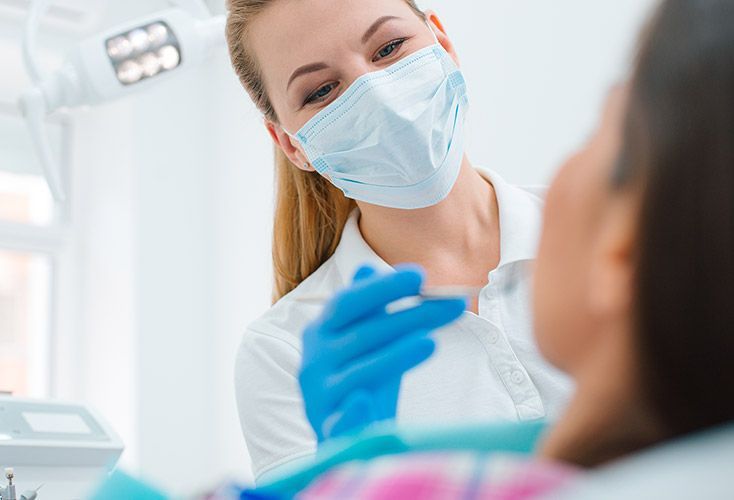 A female dentist is examining a patient 's teeth in a dental office.