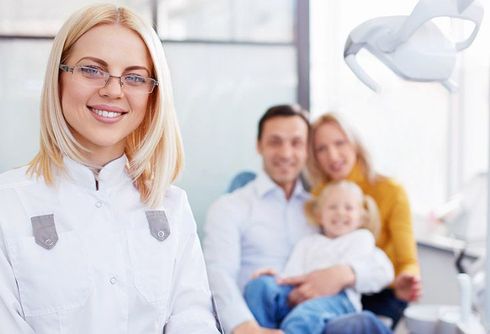 A female dentist is smiling in front of a family in a dental office.