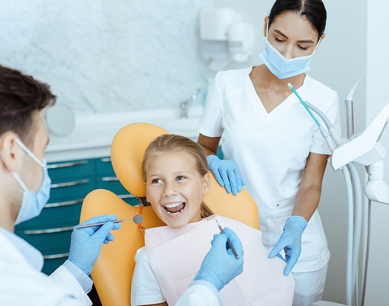 A little girl is sitting in a dental chair while a dentist examines her teeth.