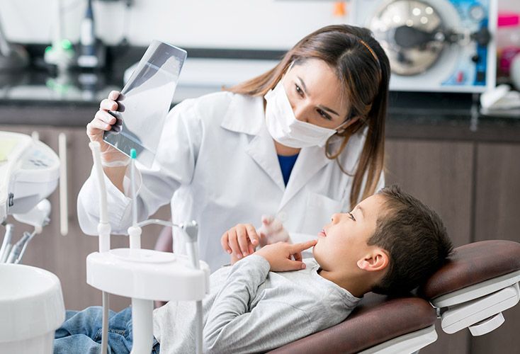A young boy is sitting in a dental chair while a dentist examines his teeth.