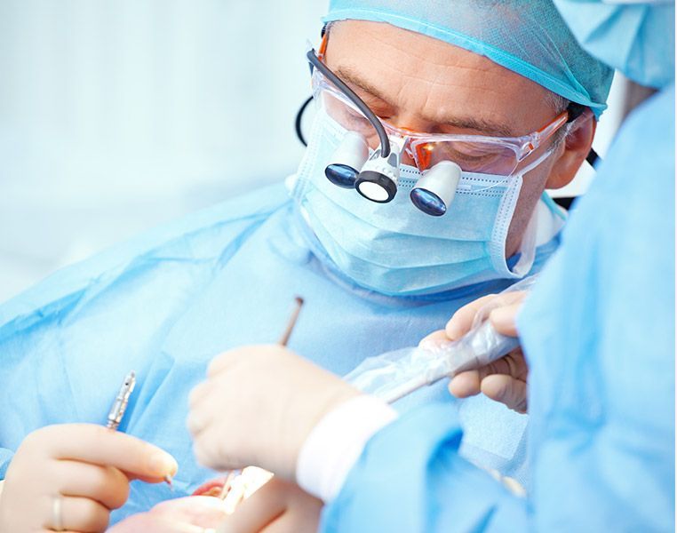 A surgeon wearing a mask and glasses is operating on a patient
