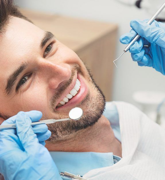 A man is smiling while having his teeth examined by a dentist.