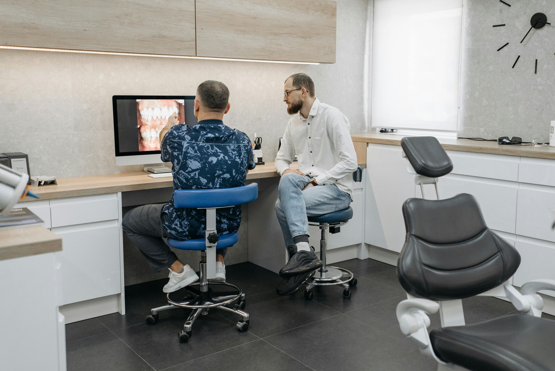 Two men are sitting in a dental office looking at a computer screen.