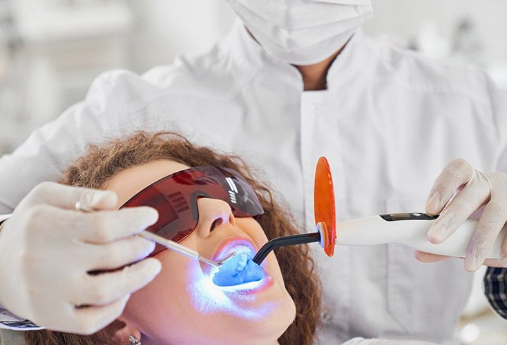 A woman is getting her teeth whitened by a dentist.