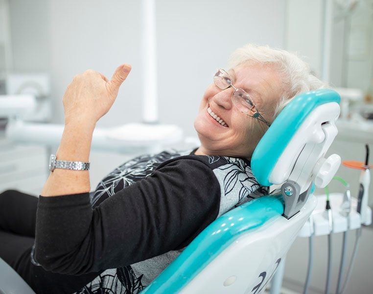 An elderly woman is sitting in a dental chair and smiling.