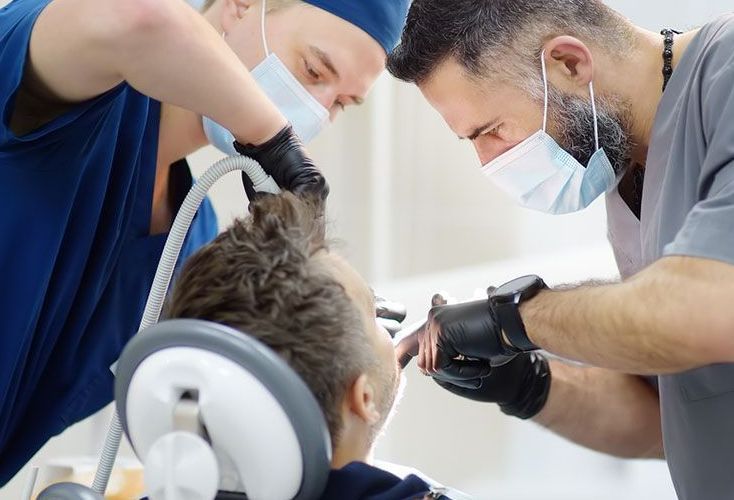 Two dentists are examining a patient 's teeth in a dental office.