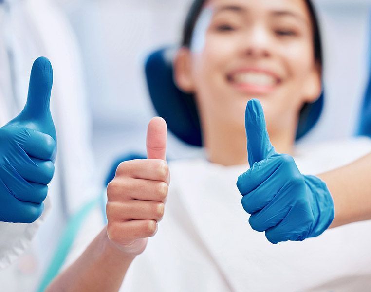 A woman in a dental chair is giving two thumbs up.