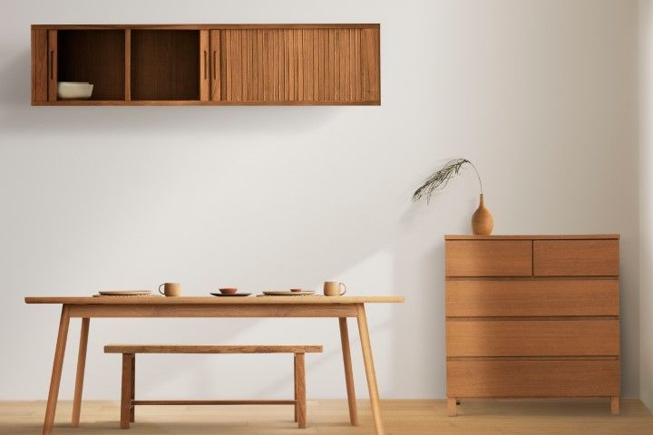 Dining room with wooden furniture: table, bench, cabinet, and chest of drawers. White walls, natural light.