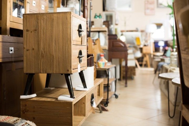 Wooden cabinet with black legs on display in a store, shelves and other furniture in background.